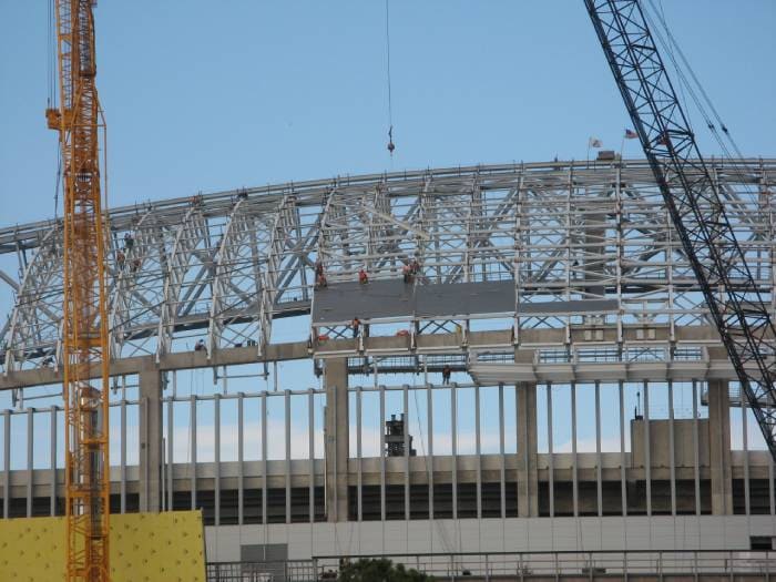 Steel stadium framework under construction with cranes and roof supports