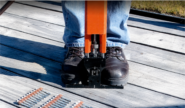 Worker using a pneumatic fastening tool to install truck and trailer flooring with fasteners staged nearby