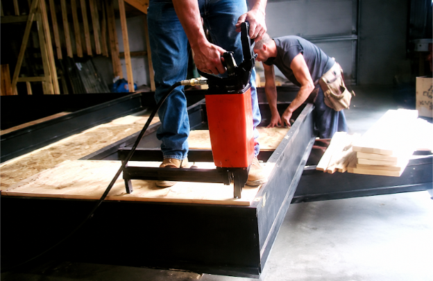 Crew members using pneumatic fastening equipment to assemble a steel modular frame